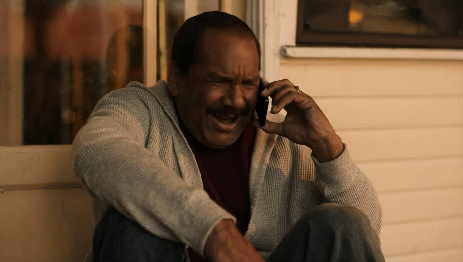 A man in his forties sitting alone on a porch step at golden hour, eyes closed, phone held gently to his ear, mid conversation with someone he loves